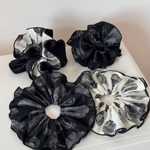 Detail of four pleated hair scrunchies in black and white patterns with silky texture