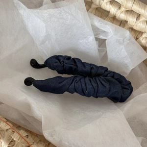 Detail der dunkelblauen Banana-Haarklammer aus Denim auf gewebtem Korb-Hintergrund