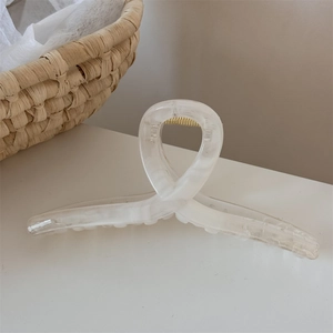 Dettaglio di una pinza per capelli in resina crema con trama marmorea e molla oro