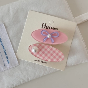 Détail de pinces à cheveux fleuries roses avec nœuds 3D et perles sur carte de marque
