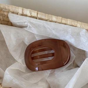 Macro detail of amber brown resin hair claw clip in a woven basket with minimalist design