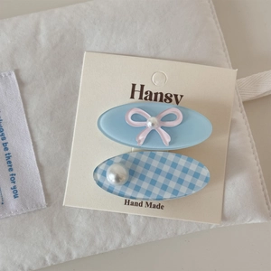 Détail de barrettes bleu ciel avec nœud en ruban rose et perles sur support carton