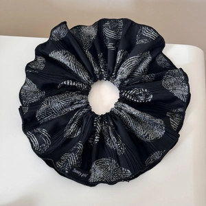 Detailed view of black pleated hair scrunchie with white shell patterns and brand label