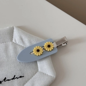 Detailopname van lichtblauwe haarclip met twee gele zonnebloemen op witte stof