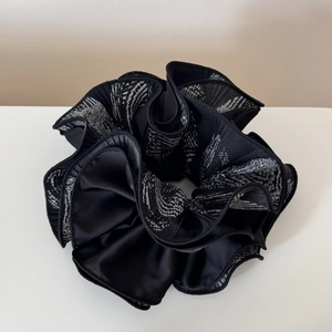 Close-up of a large black pleated scrunchie with white woven texture and glossy finish