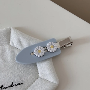 Detailopname van een blauwe acetaat haarclip met twee kleine witte madeliefjes als decoratie