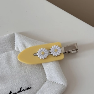 Detailopname van de gele acetaat haarklem met twee witte madeliefjes als decoratieve accenten