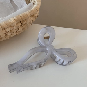 Detail of elegant marble texture hair claw clip with golden spring on a soft cream surface