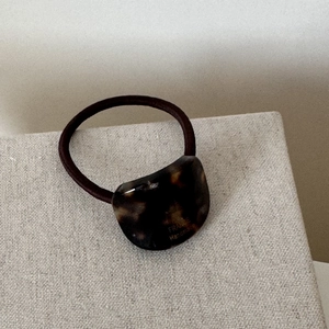 Detail of tortoiseshell hair tie with France Handmade gold lettering on beige surface