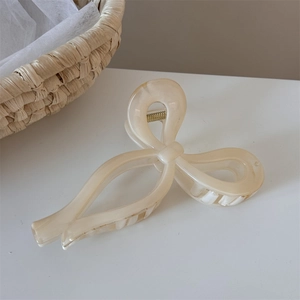 Close-up of a cream-colored ribbon bow hair claw clip with elegant marble texture and metal spring