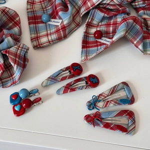 Close-up of red and blue plaid hair clips with heart and bow details on white background