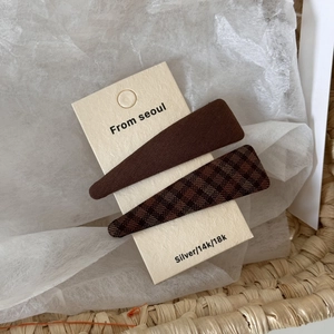 Detail view of brown fabric and plaid hair clips on a display card with Korean style aesthetics
