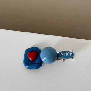 Detail of blue resin hair clip featuring red heart patterns and silver metal duckbill base