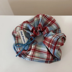 Detailed macro of red and blue plaid scrunchie with a blue bow and heart charm