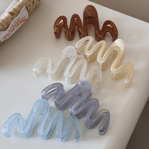 Five assorted wavy claw clips in earthy and pastel tones on a minimalist background