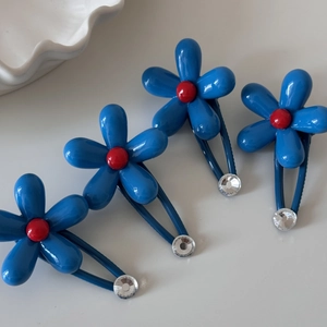 Set of 4 blue flower hair clips with red centers and rhinestones on grey background