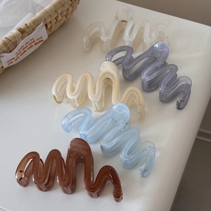 Detail view of wavy resin hair claws in five colors on white surface with basket