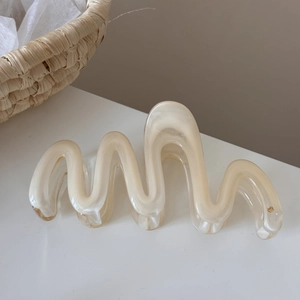 Macro detail of wave-shaped hair claw clip in translucent cream resin with glossy finish