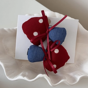Close-up of red polka dot and blue denim bow hair clips in a white ceramic bowl