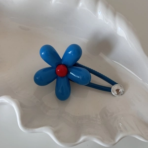 Detail view of blue flower hair clip with red center and rhinestone on white shell tray