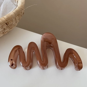Macro shot of wavy brown resin hair claw clip with a glossy finish on white surface