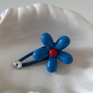 Detail of blue flower hair clip with a red center and sparkling rhinestone on a white plate