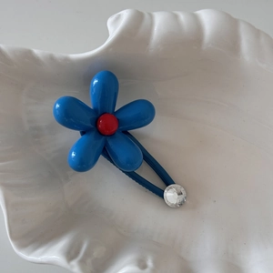 Close-up of a blue flower hair clip with a red bead center and rhinestone on a shell tray