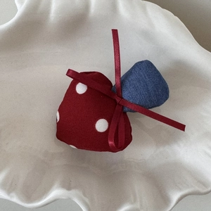 Detailed close-up of red polka dot mushroom hair clip with deep red satin ribbon on tray