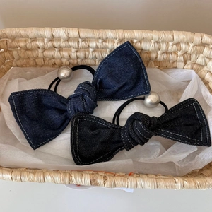 Detail of denim bow hair ties with white stitching and decorative silver beads