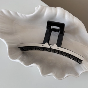 Détail d'une pince à cheveux noire chic avec un motif d'ours blanc sur un plat en céramique