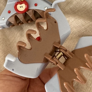 Detail showing the gray and brown hair claw with a red apple charm and shiny rhinestones
