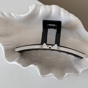 Détail d'une pince à cheveux noire avec motif de chat mignon posée sur un plat en coquille