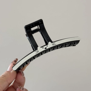 Détail de la pince à cheveux noire brillante avec un motif minimaliste de chat blanc