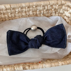 Detailed view of denim bow hair tie with white stitching and silver bead accent