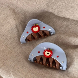Detail of light blue hair claw clips with 3D red apple design and sparkling rhinestones