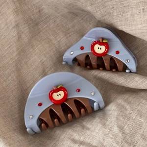 Blue semi-circle hair claw clip with red apple charm and crystals on beige fabric