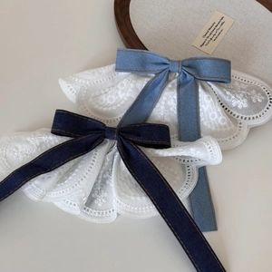 Close-up of white floral embroidery lace shawl with denim bow and fine stitching details