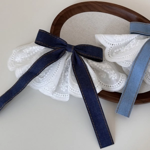 Detail of denim bow hair clip featuring white lace embroidery and long ribbon tails