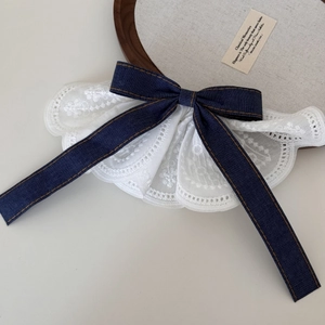 Detail of white embroidery lace collar with a large navy denim bow and brown topstitching