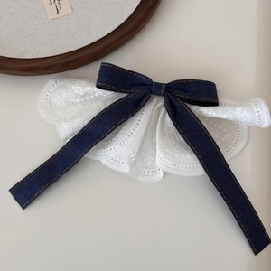 Detail of a denim bow hair clip with white lace trim and vintage brown stitching accents