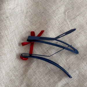 Détail d'une pince à cheveux bec de canard bleu foncé avec nœud rouge et bouton coeur