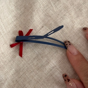 Détail d'une pince à cheveux bleue avec un nœud papillon rouge sur fond de toile