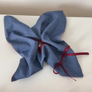 Close-up detail of denim blue hair scrunchie with red lining and a satin ribbon bow