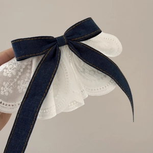 Detailed macro view of denim bow hair clip with white lace embroidery and yellow stitching
