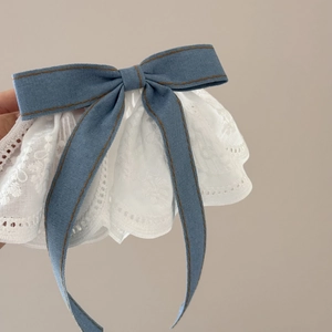 Detail of blue denim bow hair clip with white floral lace trim and brown stitching