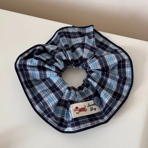 Détail d'un chouchou à carreaux bleus avec écusson Sweat Dog et accent de bouton bleu
