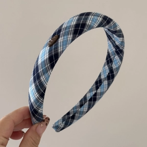 Détail d'un serre-tête rembourré à carreaux bleus avec écusson métallique du logo de la marque