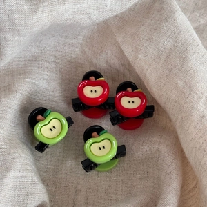 Close-up of four mini red and green apple hair clips on a soft beige linen cloth
