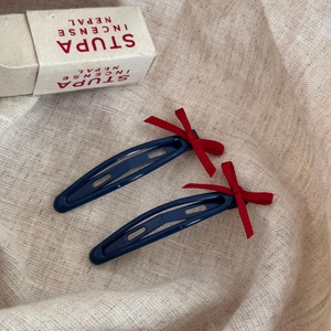 Détail des pinces à cheveux en métal bleu foncé avec des nœuds rouges sur lin