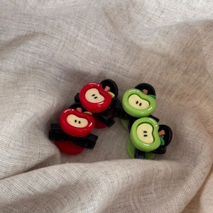 Close-up of red and green mini apple hair claws on a textured linen background